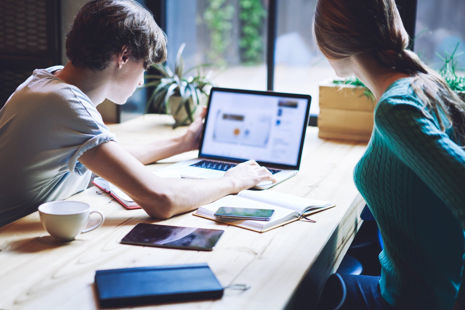 A man and a woman are sitting at a table looking at a laptop.