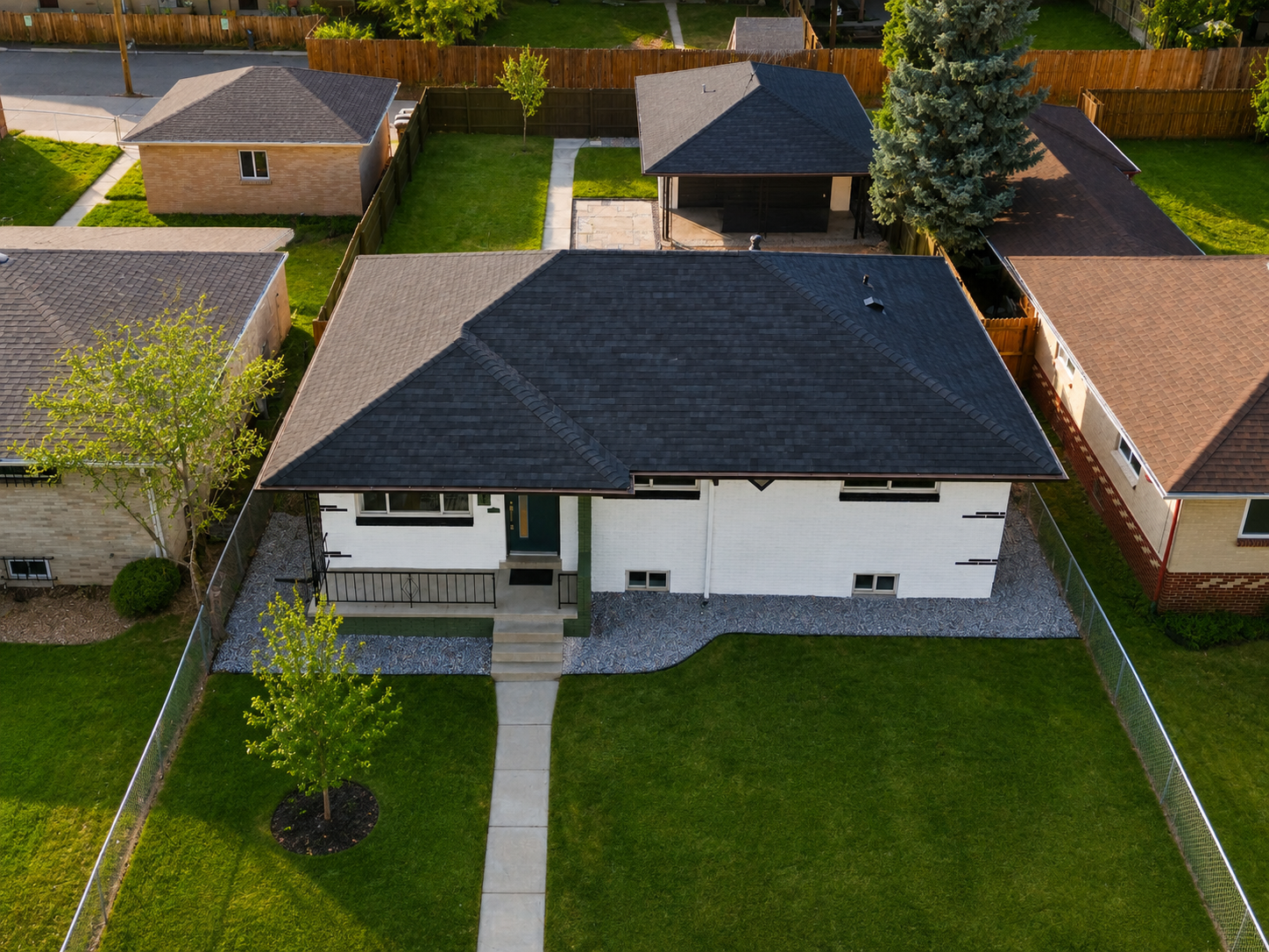 Aerial view of a white house with a dark roof and green lawn in a suburban neighborhood.