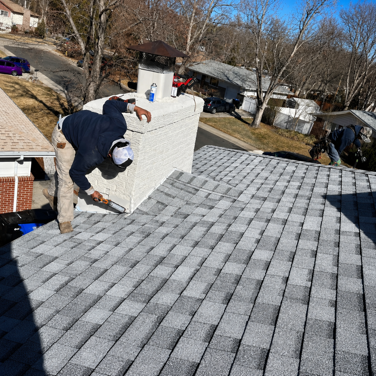 Worker installing roof shingles near a chimney on a sunlit house roof