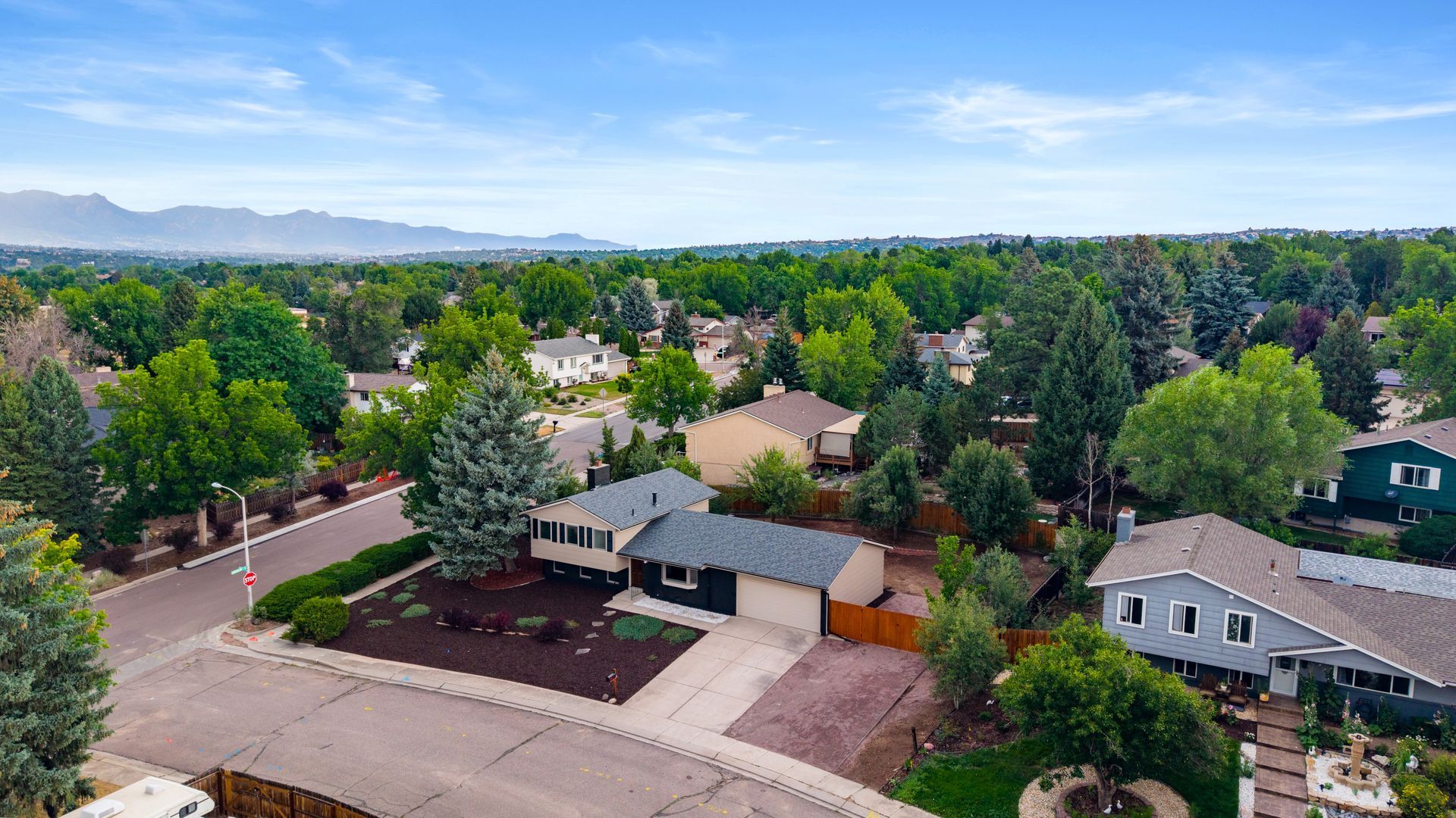 Aerial view of a suburban neighborhood with tree-lined streets, houses, and mountains in the distance