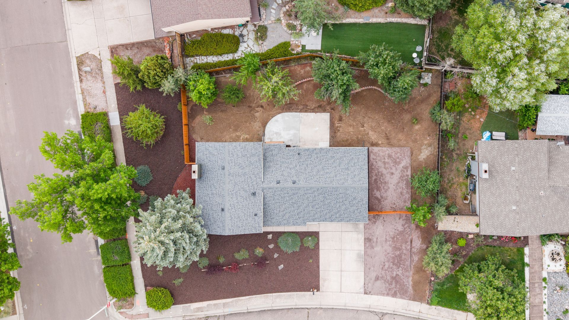 Overhead view of a house with a gray roof, driveway, and surrounding green trees and landscaping