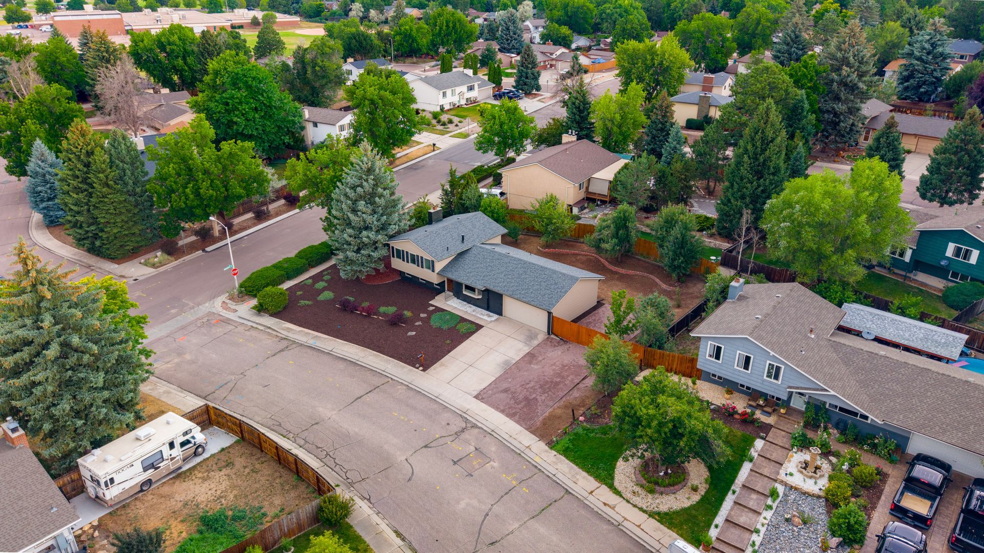 Aerial view of a suburban neighborhood with houses, streets, trees, and parked cars.