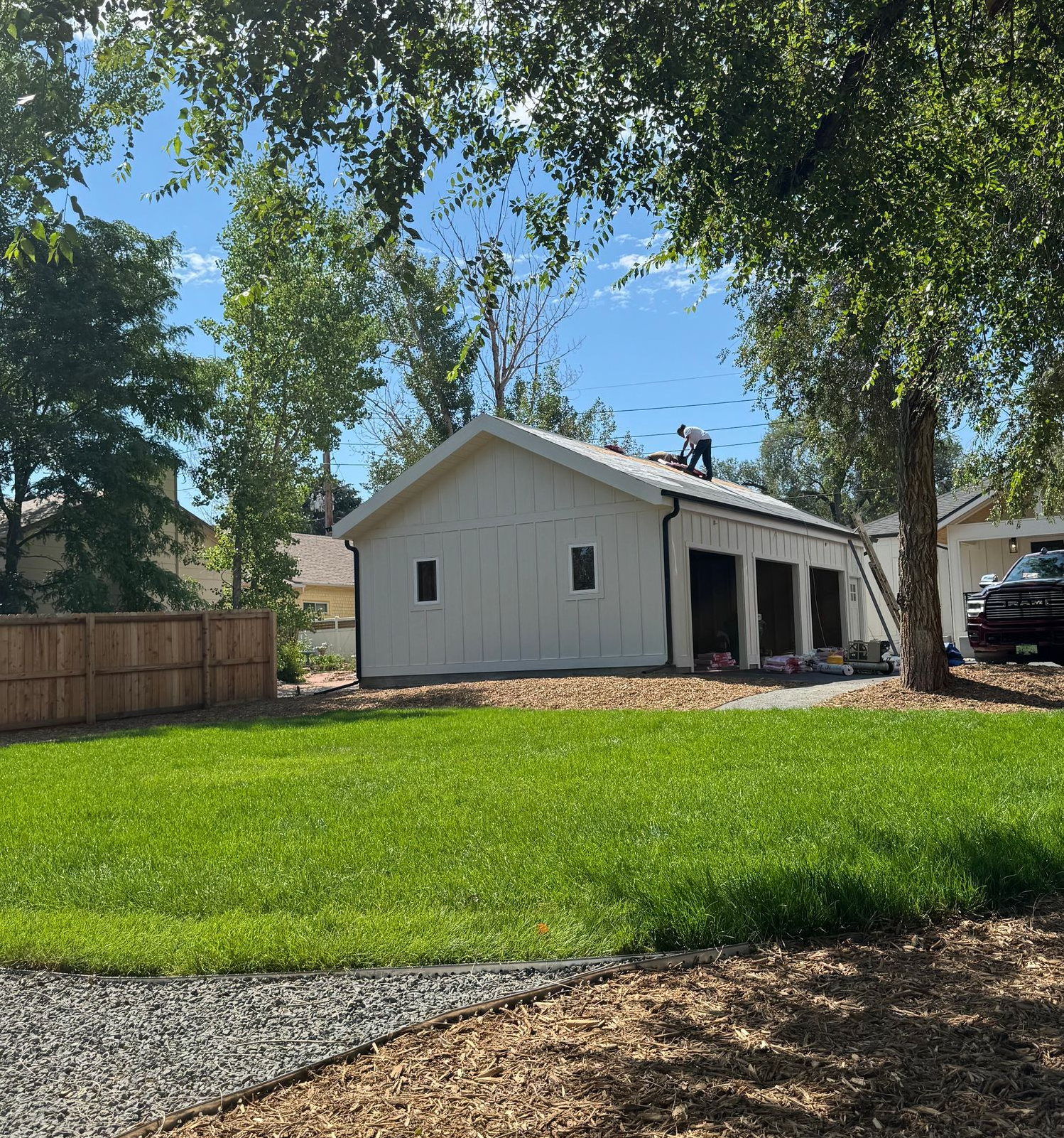 White garage with open bays beside a green lawn and tall trees on a sunny day