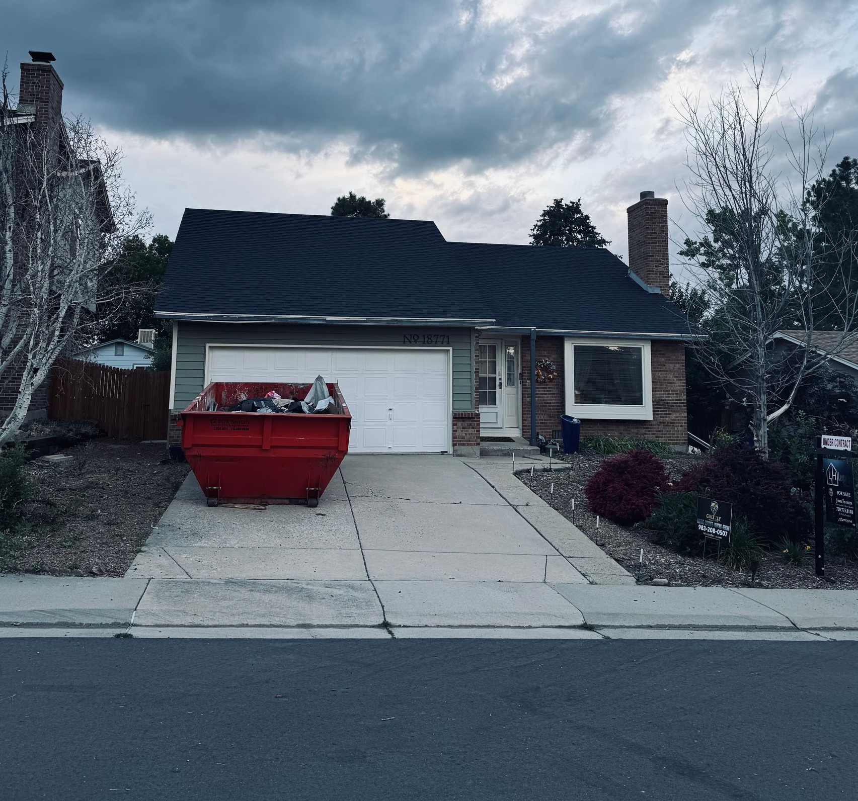 Suburban house with a driveway, red dumpster, and cloudy sky