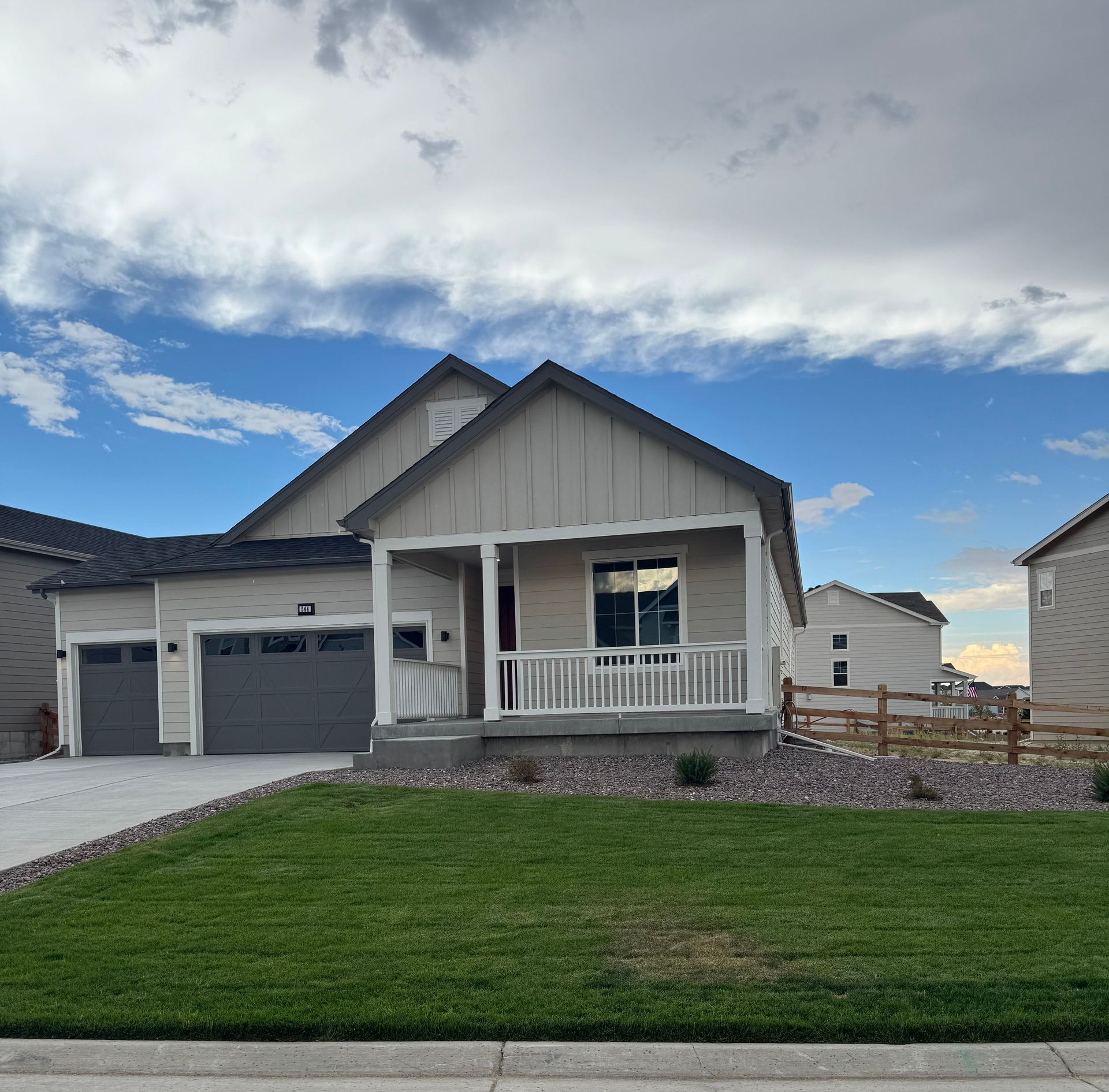 Suburban house with gray siding, front porch, garage, and green lawn under a cloudy sky