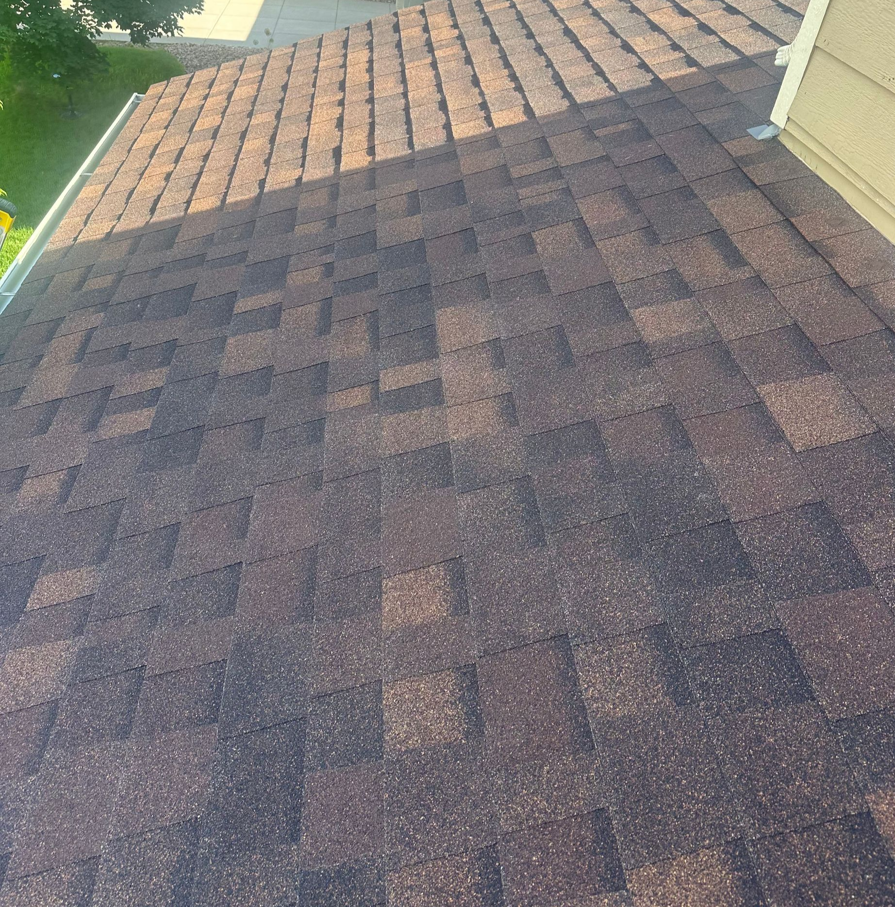 Dark asphalt shingle roof with a lighter ridge near the top and a house wall on the right