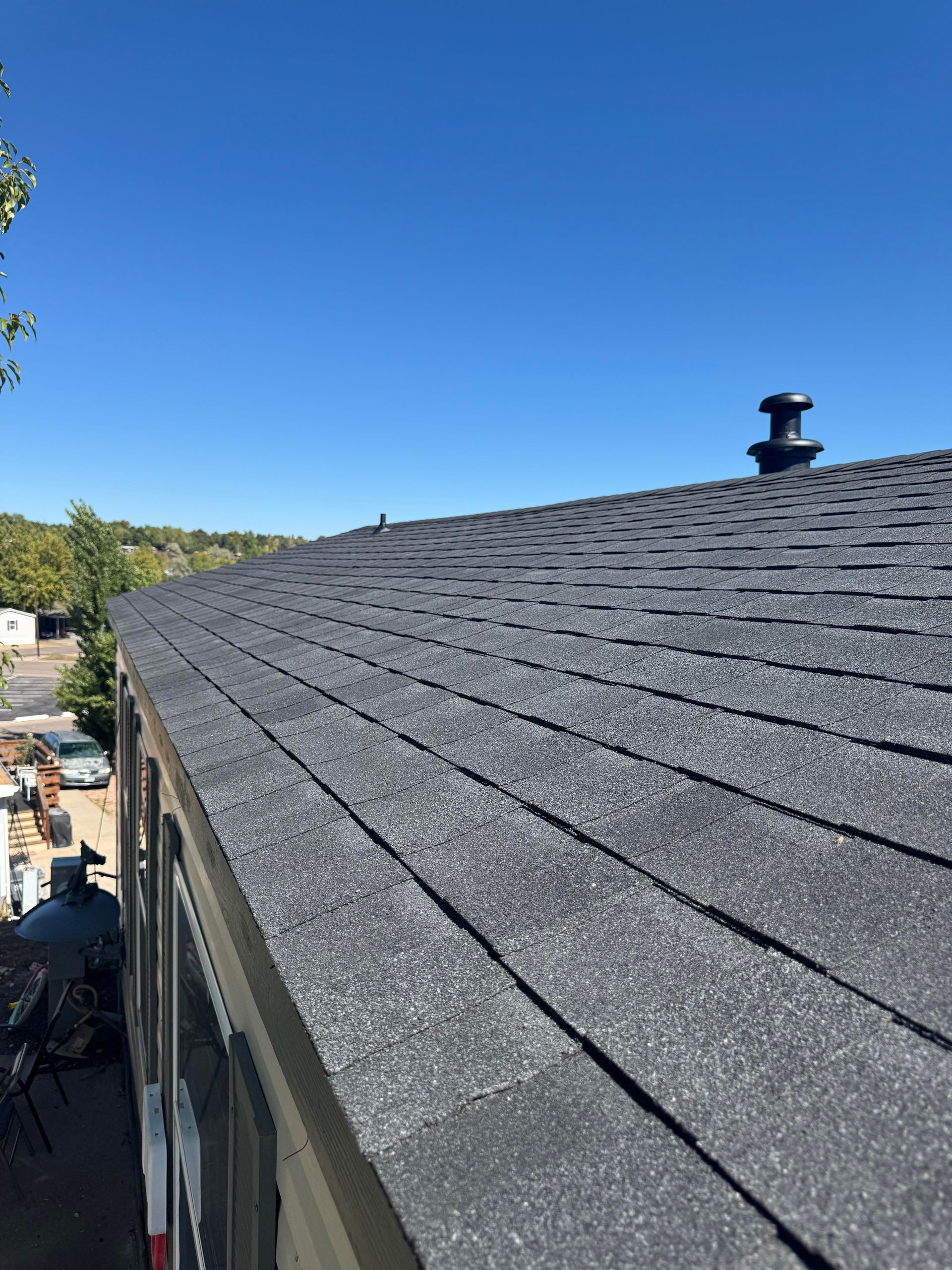 Gray shingled roof under a clear blue sky, viewed from the edge of a building
