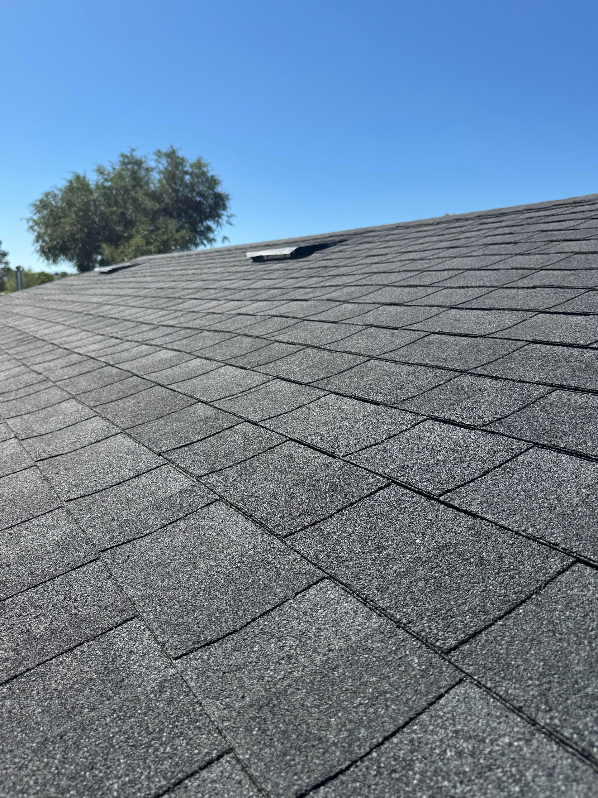Close-up of a gray shingle roof with a skylight under a clear blue sky