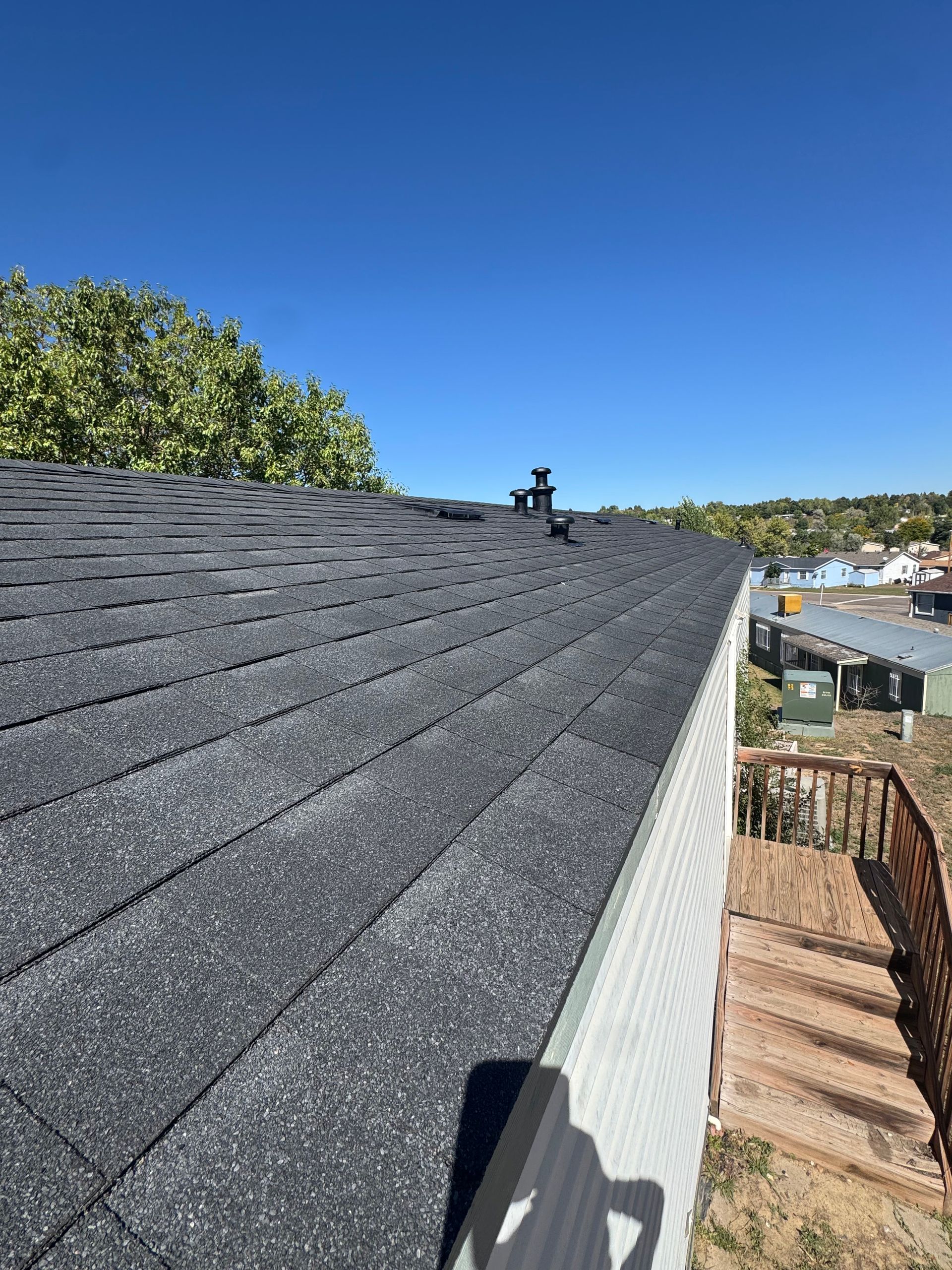 House roof with dark shingles and a vent, viewed beside a waterfront under a clear blue sky