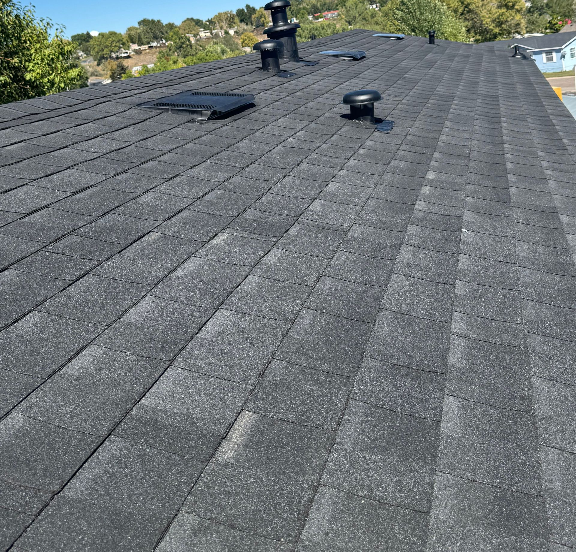 Dark gray shingled roof with vents and a skylight under a clear sky
