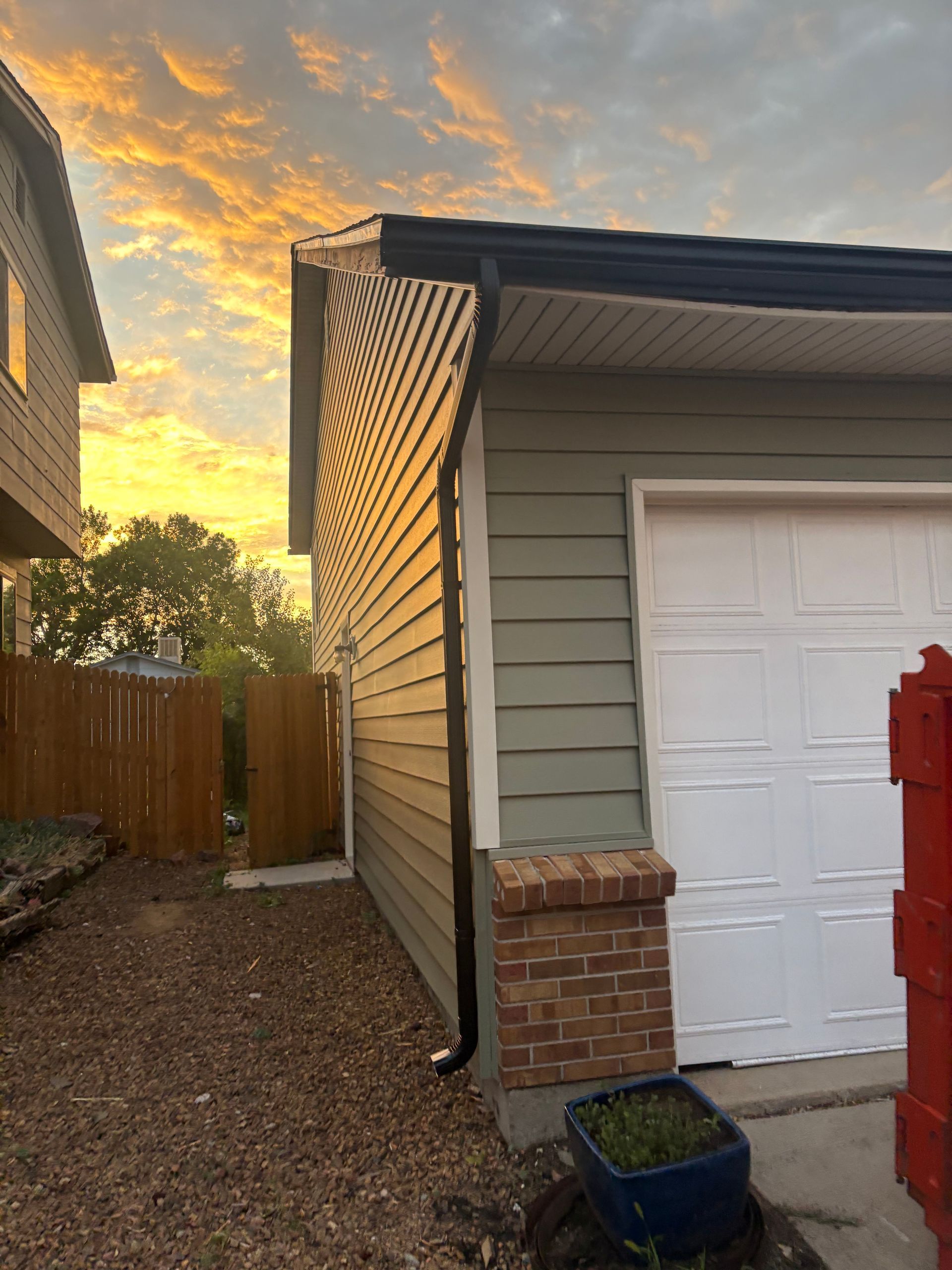Narrow side yard beside a garage at sunset, with siding, gravel, fence, and brick corner.