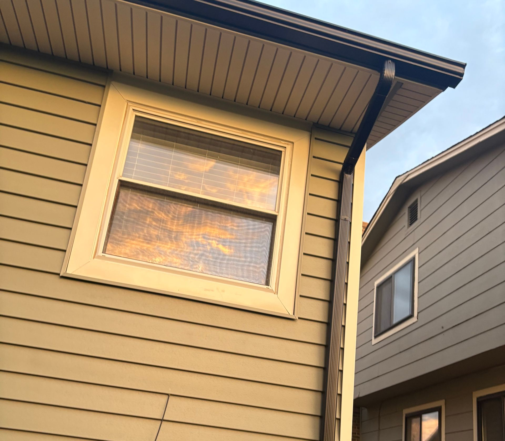 Two beige houses seen from below, with a sunlit window and roof eaves in the foreground.