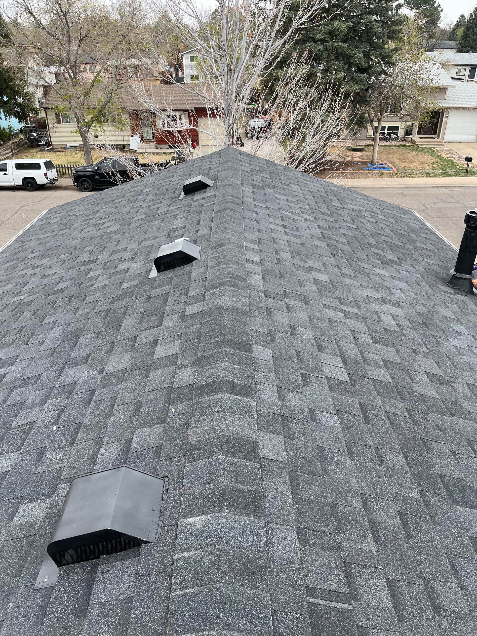 Gray shingled roof with three vents, viewed from the top toward a suburban neighborhood.