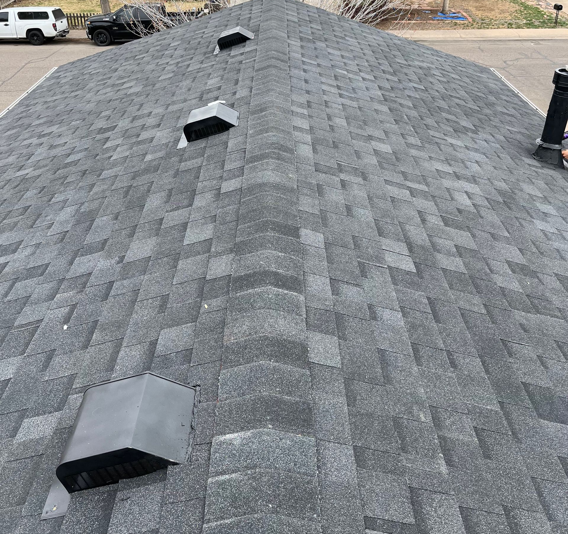 Gray shingled rooftop with three vents and a person standing at the right edge