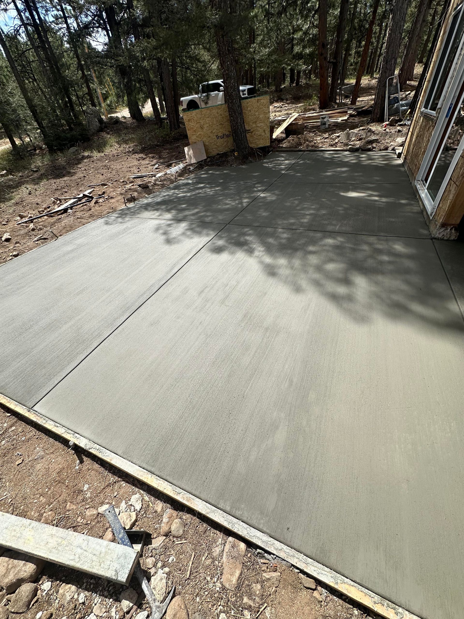 Freshly poured concrete slab in a wooded outdoor area with a small utility structure nearby