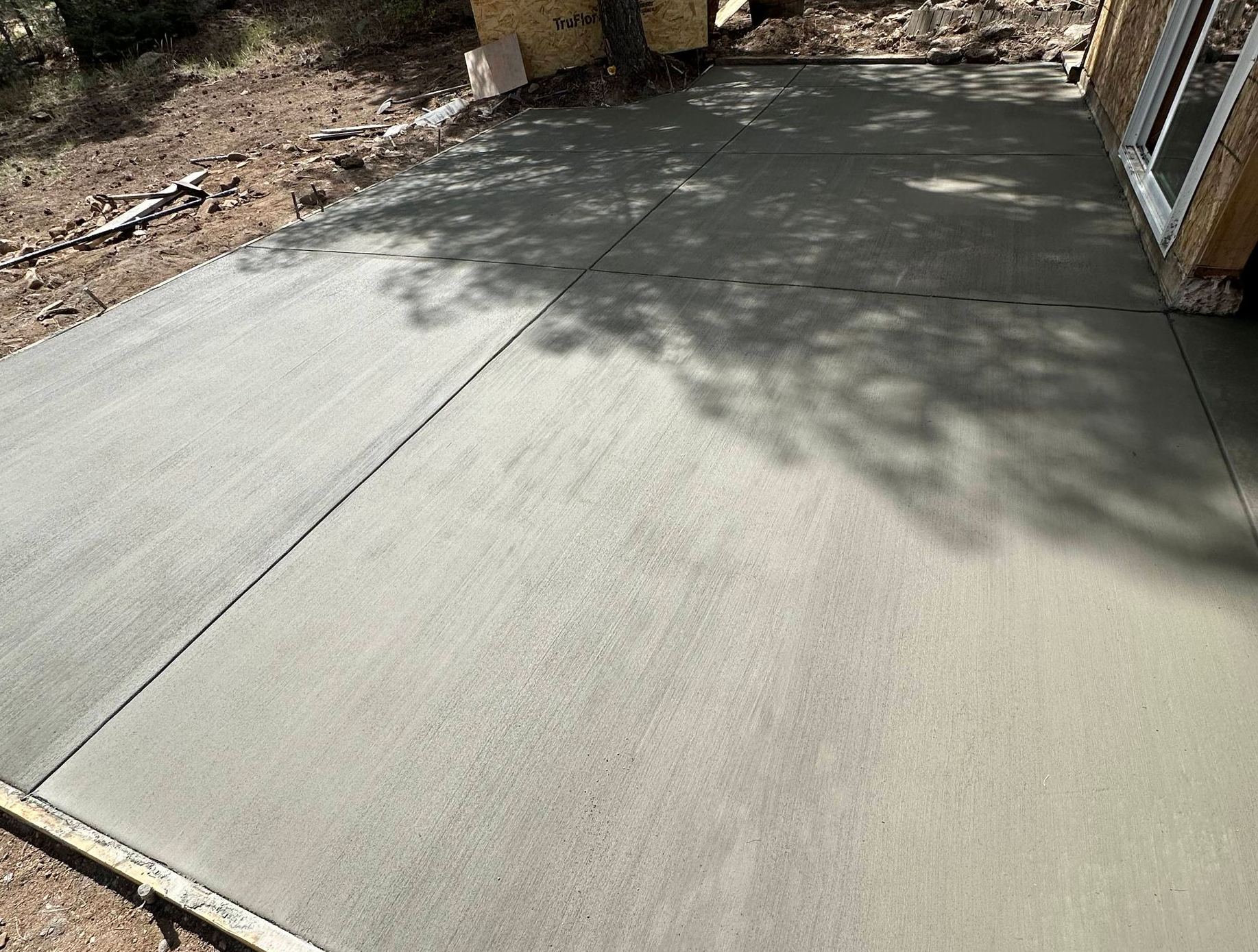 Freshly poured concrete slab beside a house, with tree shadows across the surface