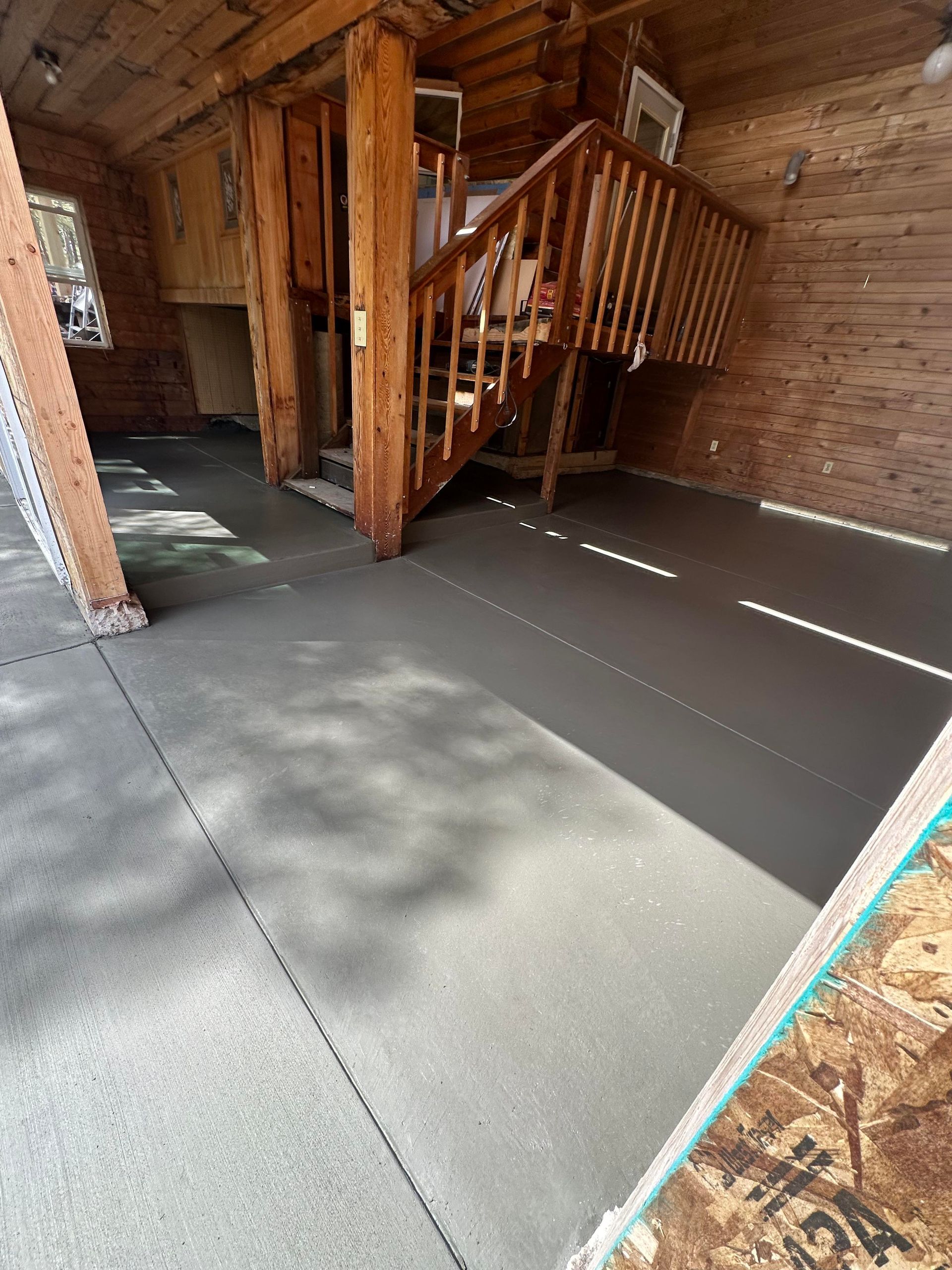 Wood-paneled cabin interior with a staircase and a newly finished gray floor near a doorway