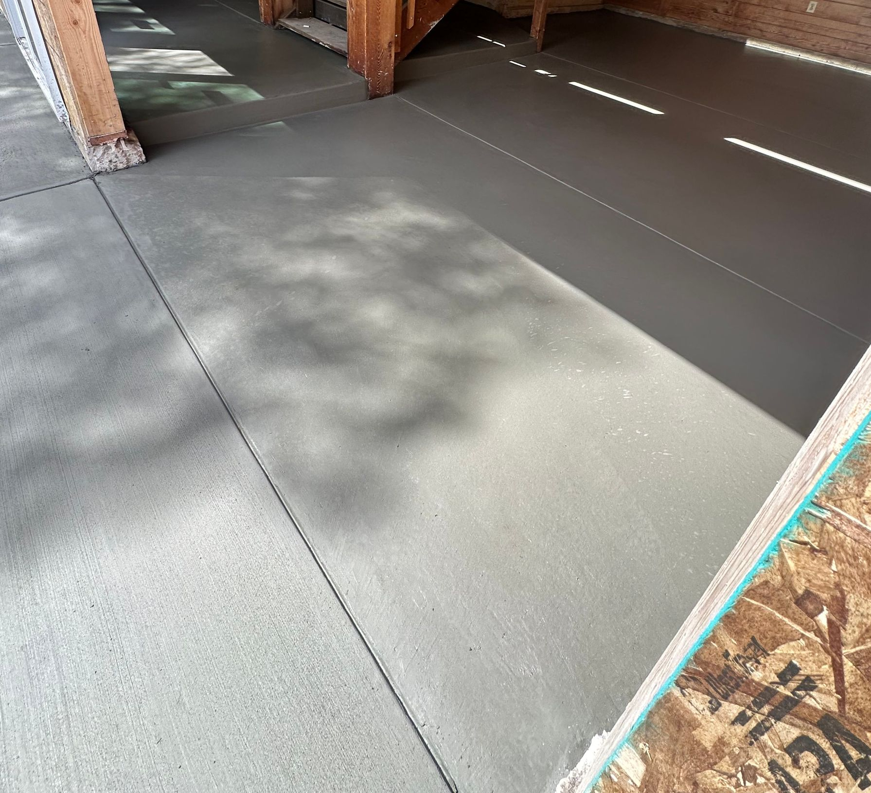 Gray concrete floor under construction with bright sunlight and shadow patterns near wood framing
