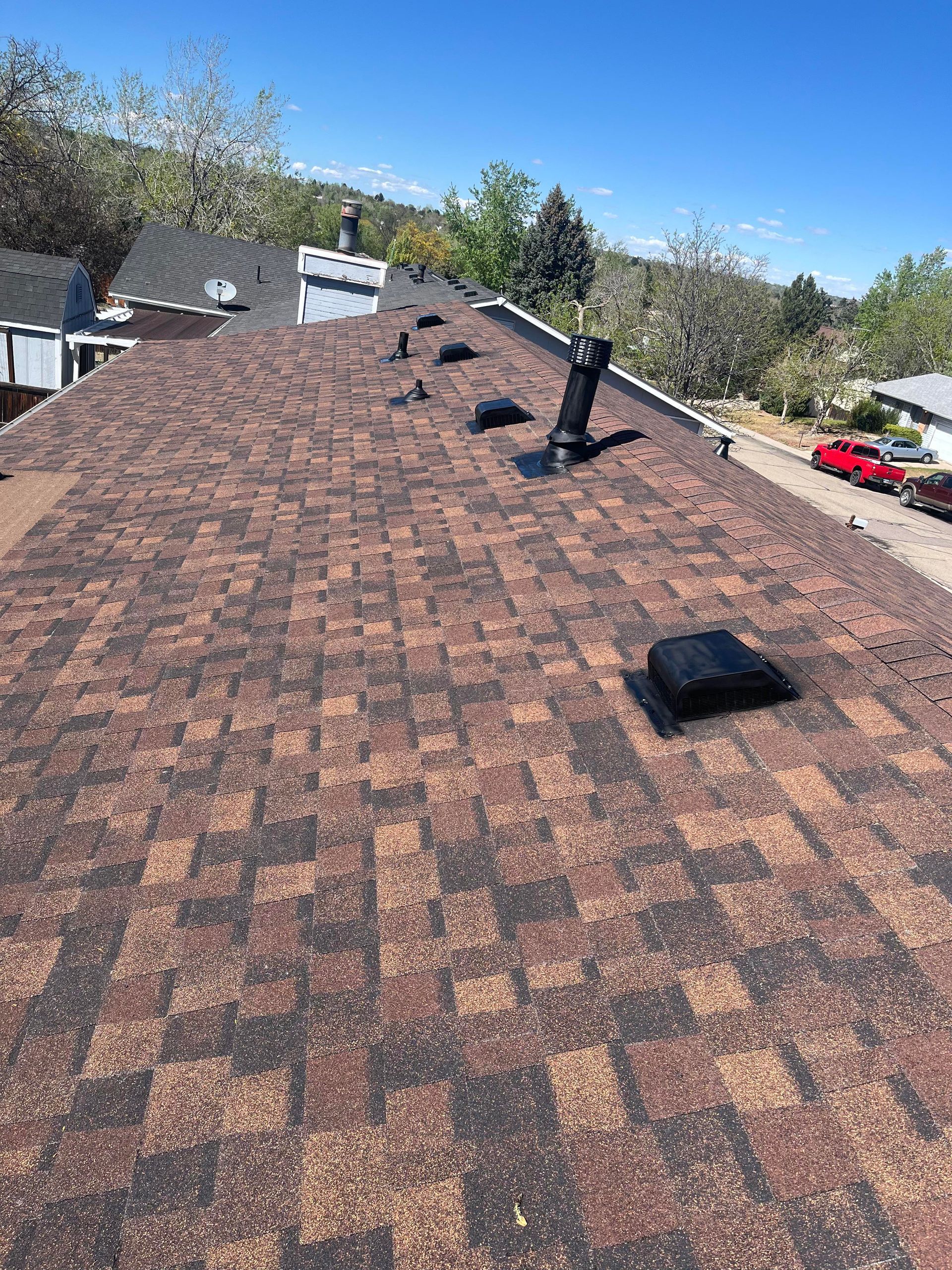 Roof with brown shingles, vents, and a small skylight under a clear sky.