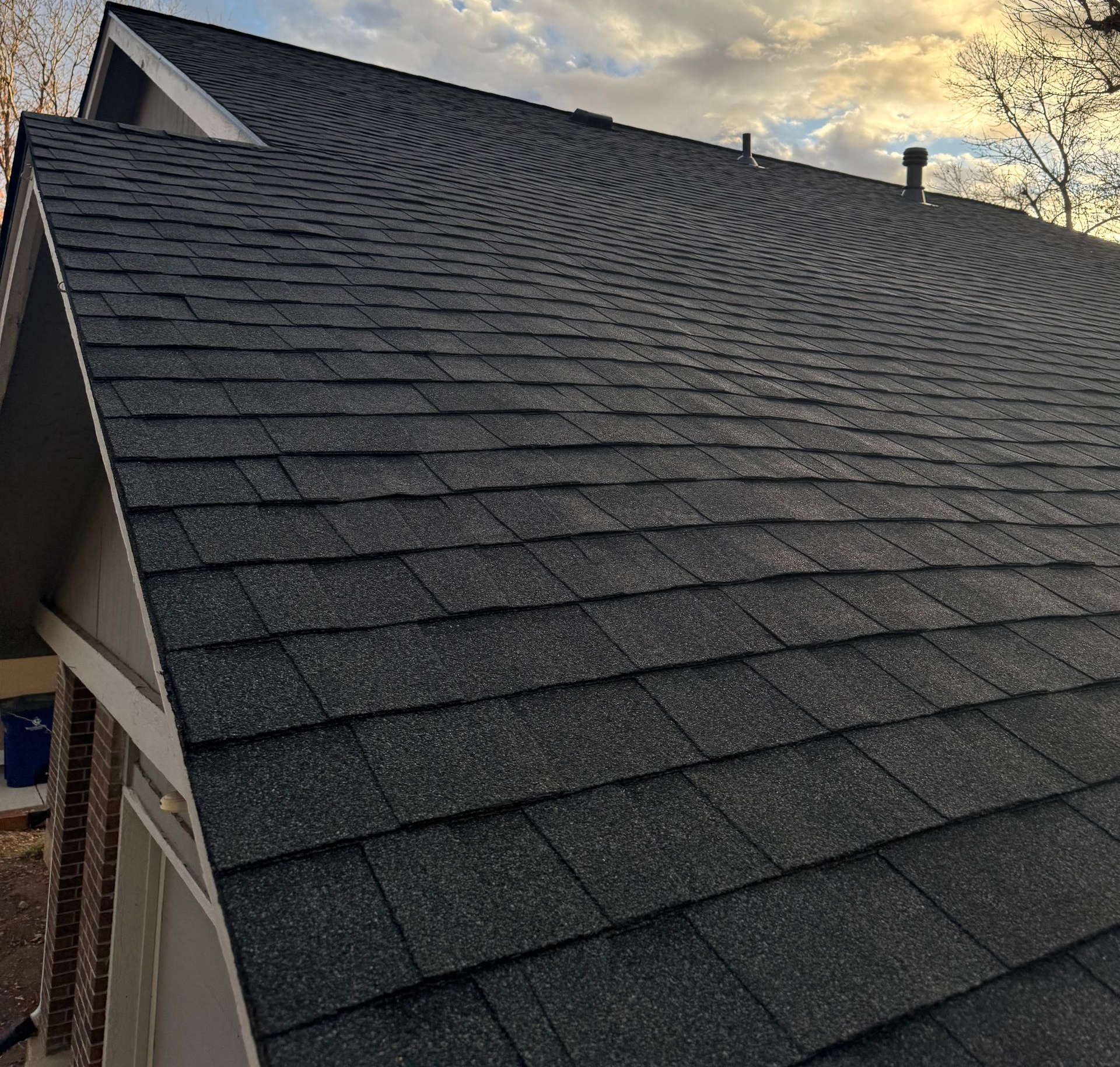 Steep dark gray shingled roof at sunset with a cloudy sky