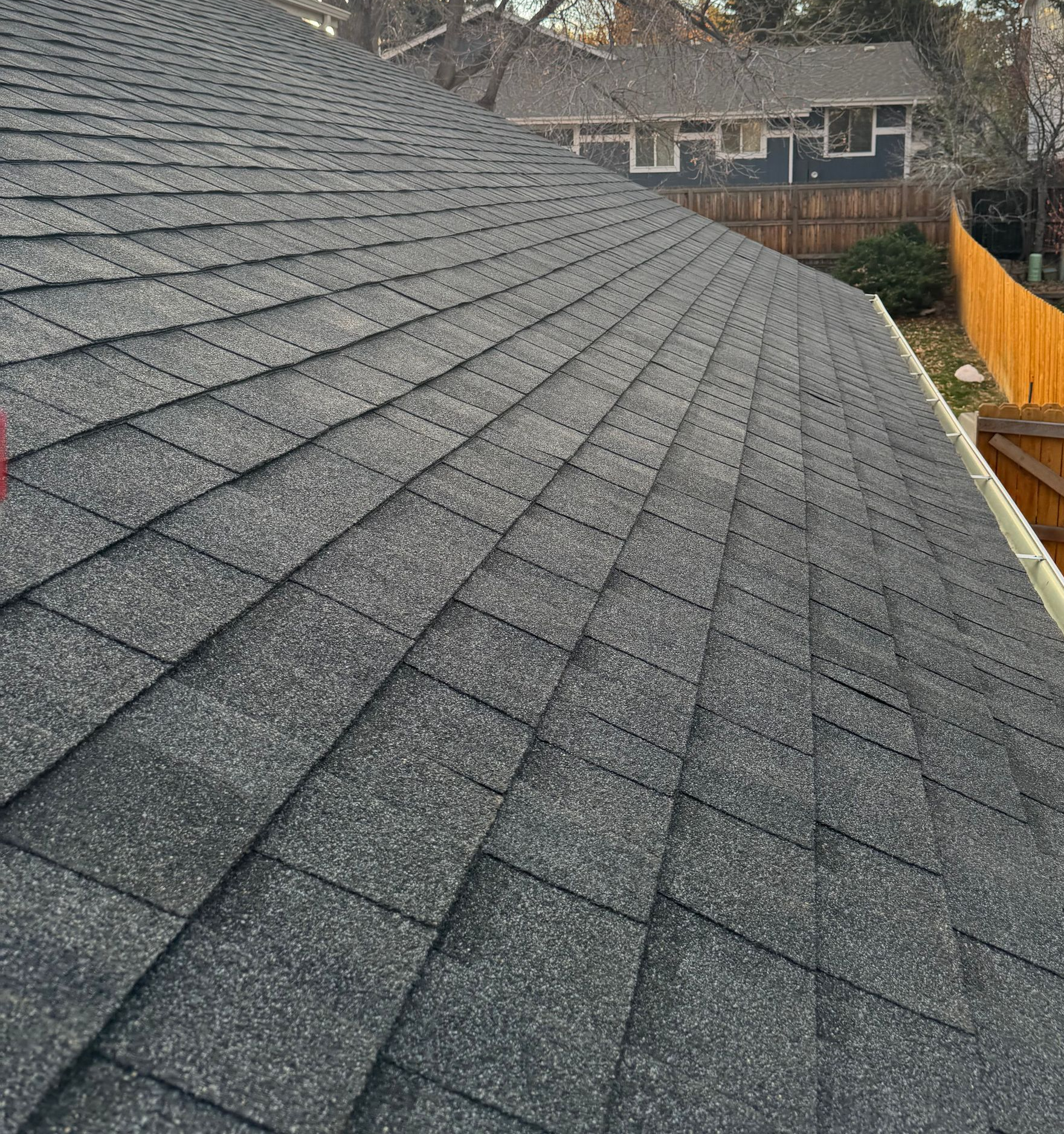 Dark gray shingled roof sloping toward a wooden fence in a suburban yard