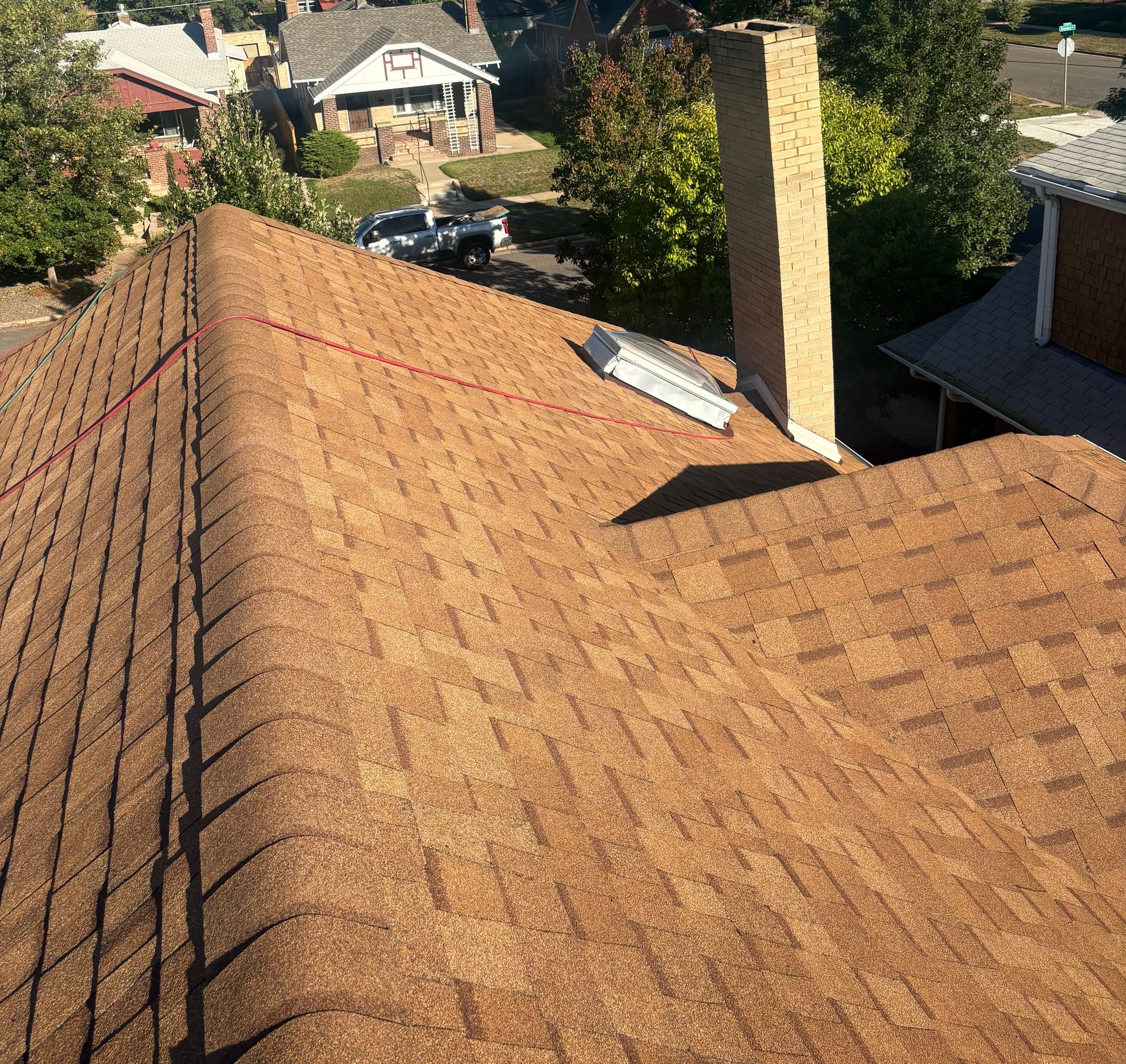 Rooftop with tan shingles, a chimney, and neighboring houses in the background