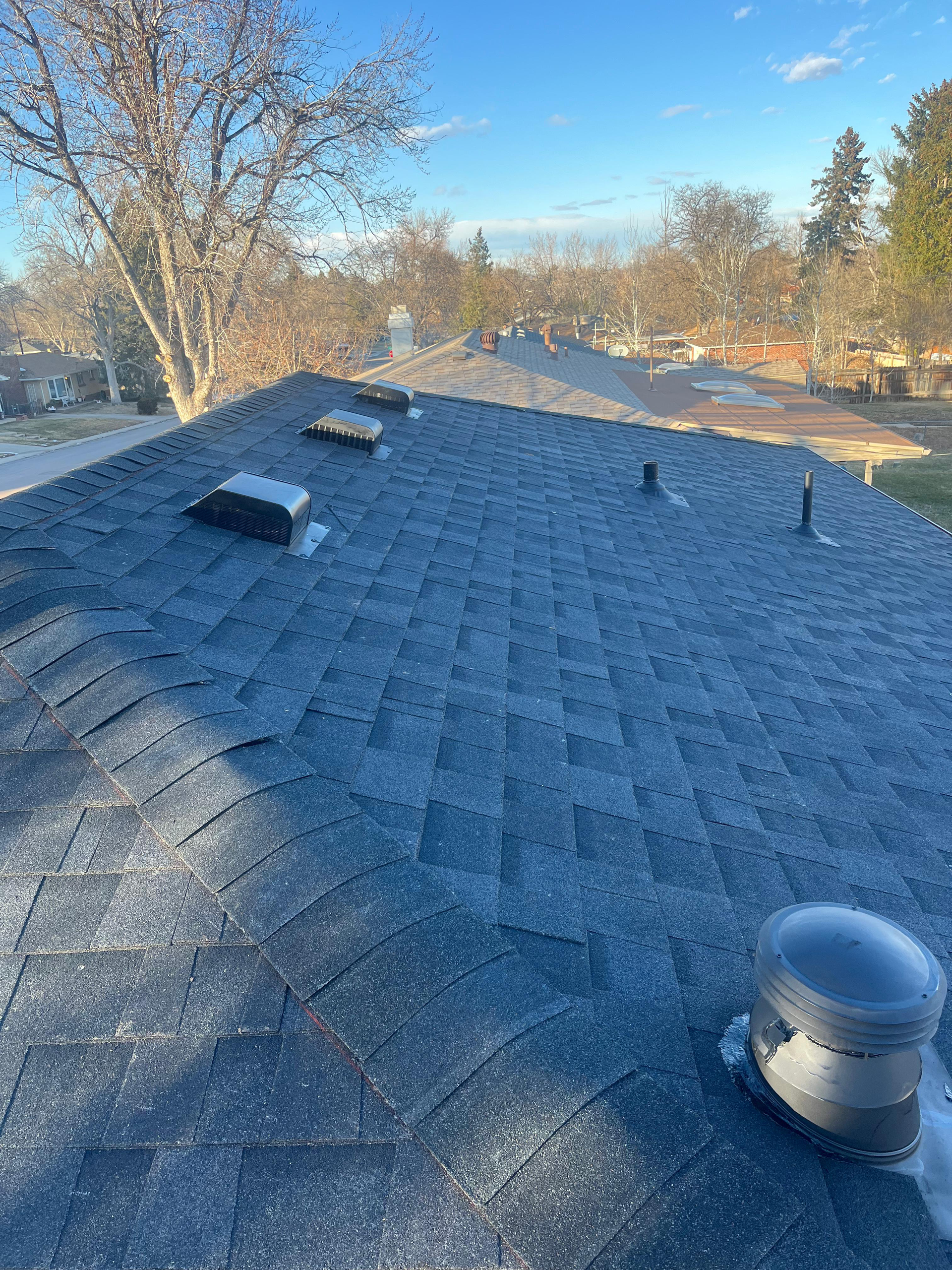 Roof with new gray shingles, vents, and a skylight under a blue sky, viewed from above.