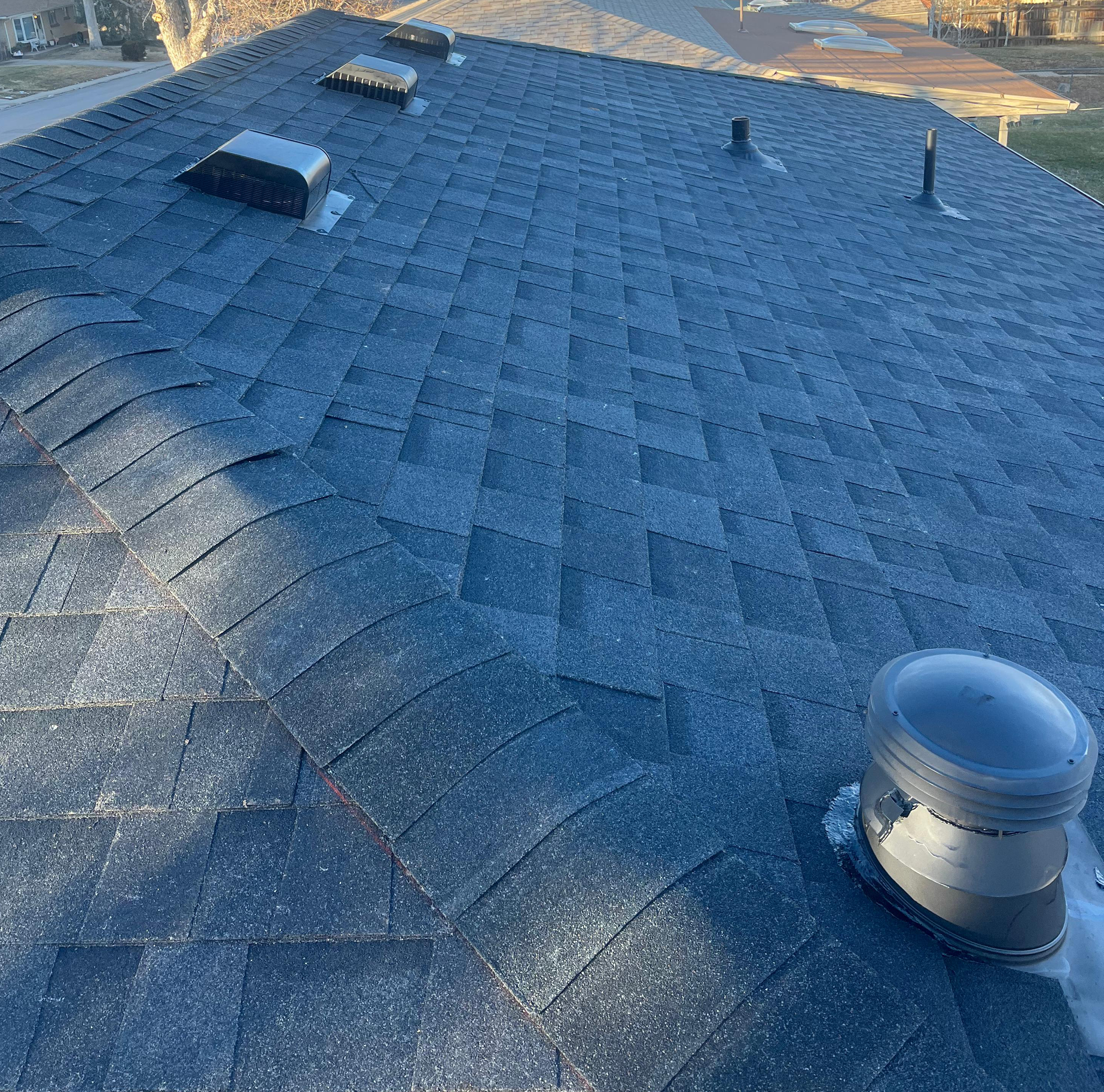Blue shingled roof with several vents and a ridge in daylight