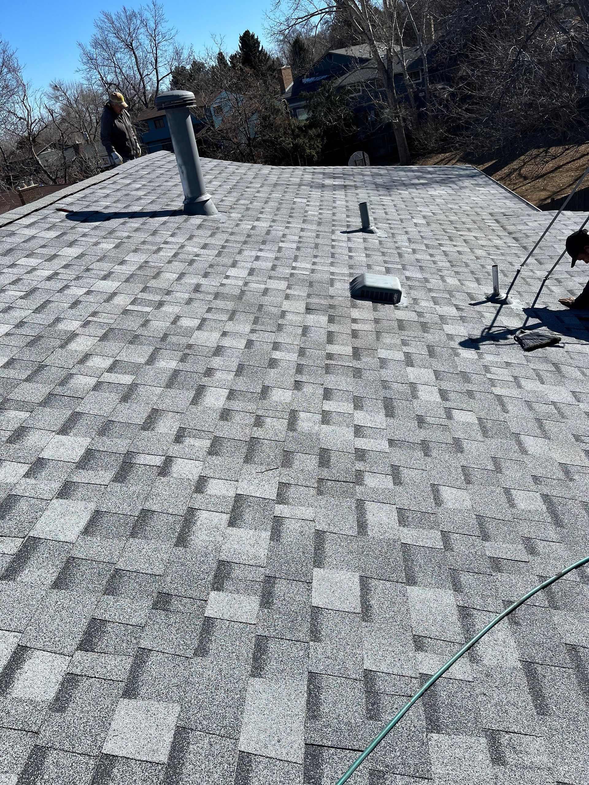 Flat rooftop with gray shingles, vents, and trees in the background.