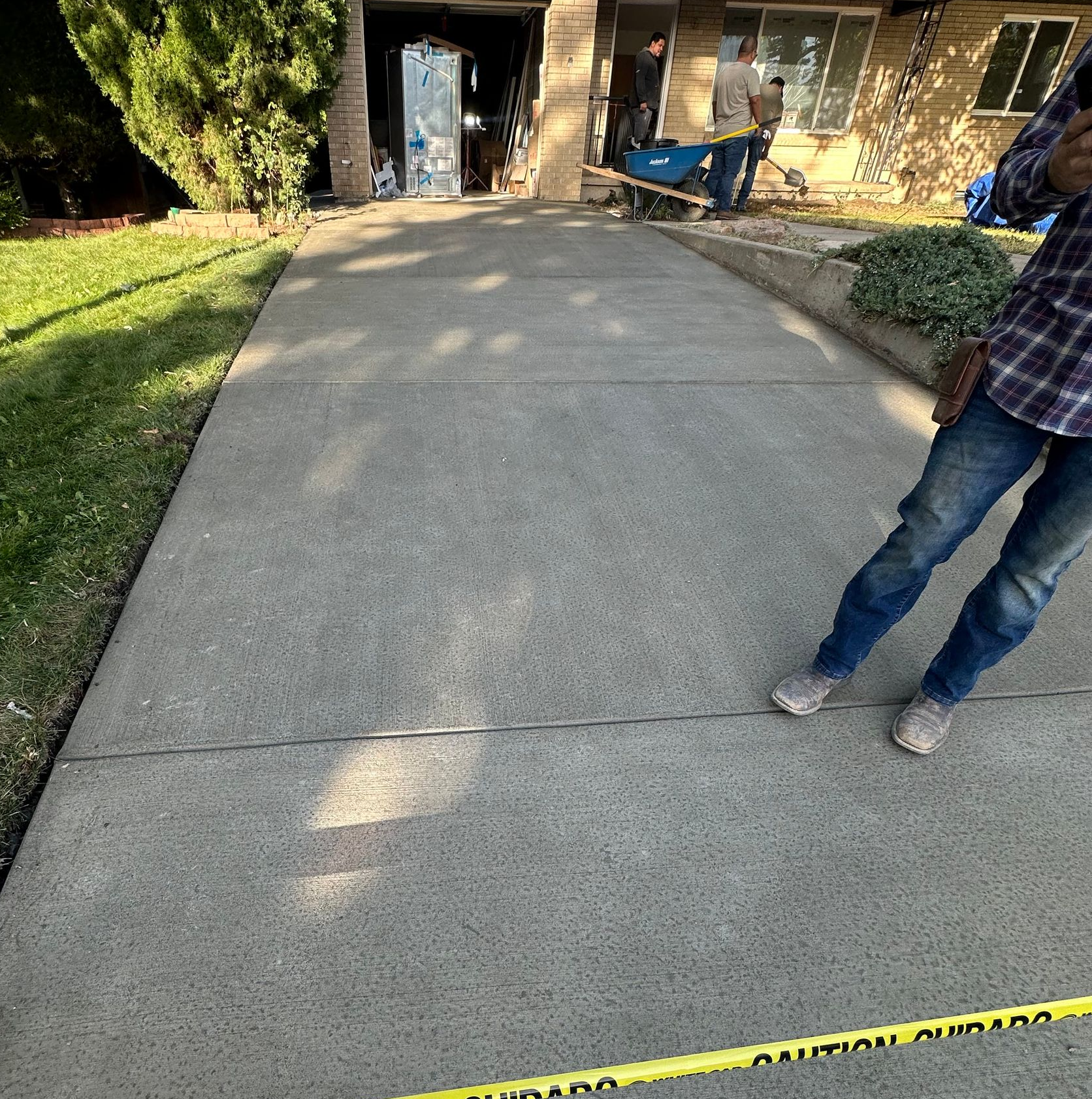 Cracked driveway leading to a house entrance, with caution tape across the bottom and a person standing at right.