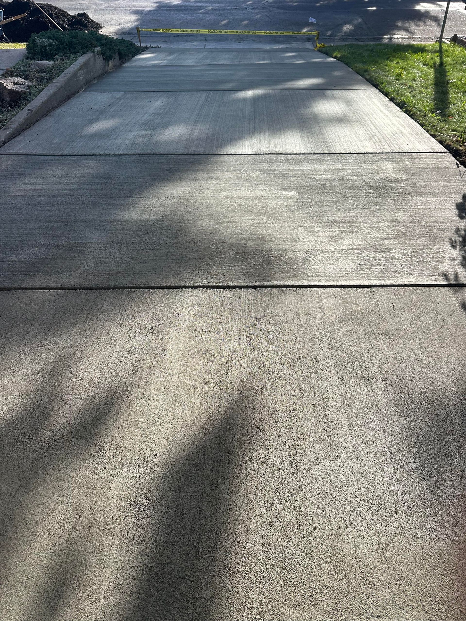 Sunlit concrete sidewalk with dark shadows from nearby trees and a grass border