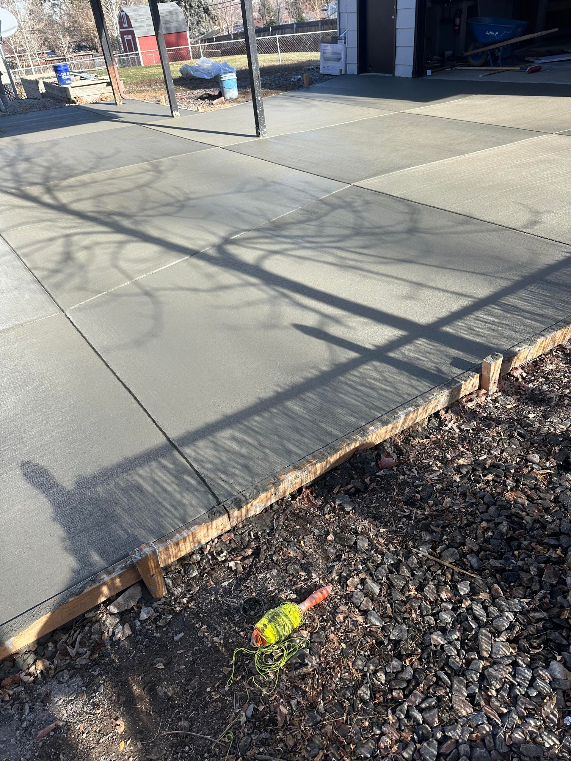 Sunlit concrete sidewalk beside a gravel bed with a small yellow-orange marker near the curb.