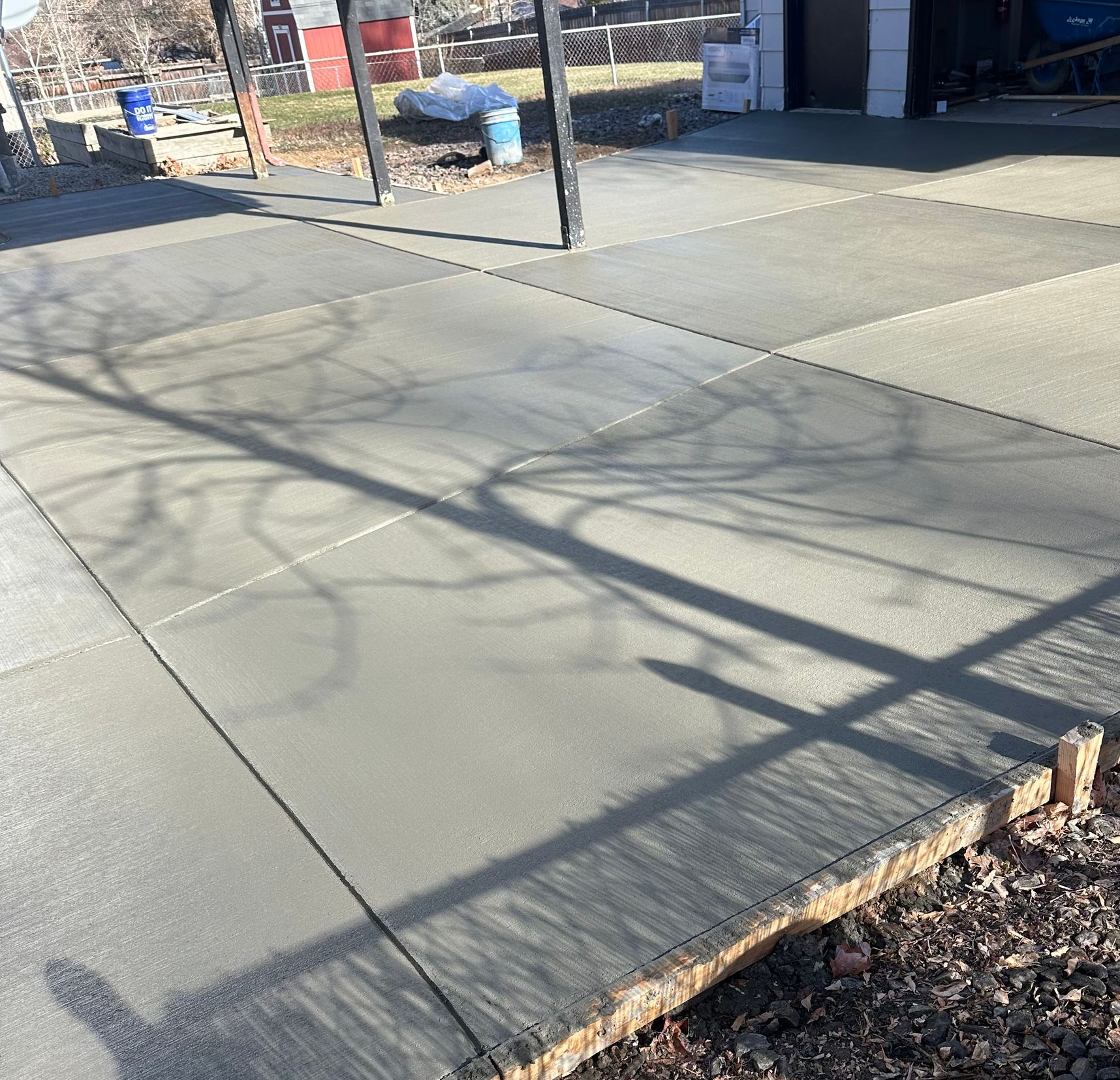 Concrete sidewalk with long tree shadows beside a brick building and garden bed