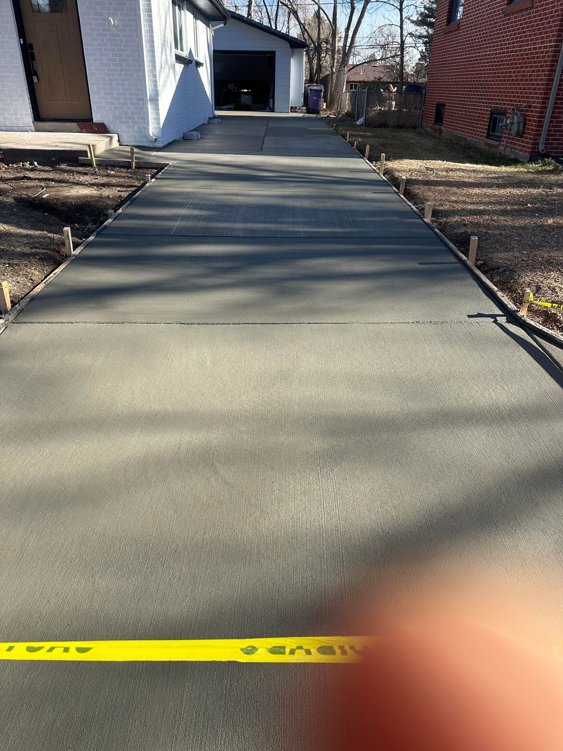 Concrete driveway leading to a garage, with yellow caution tape stretched across the bottom foreground.