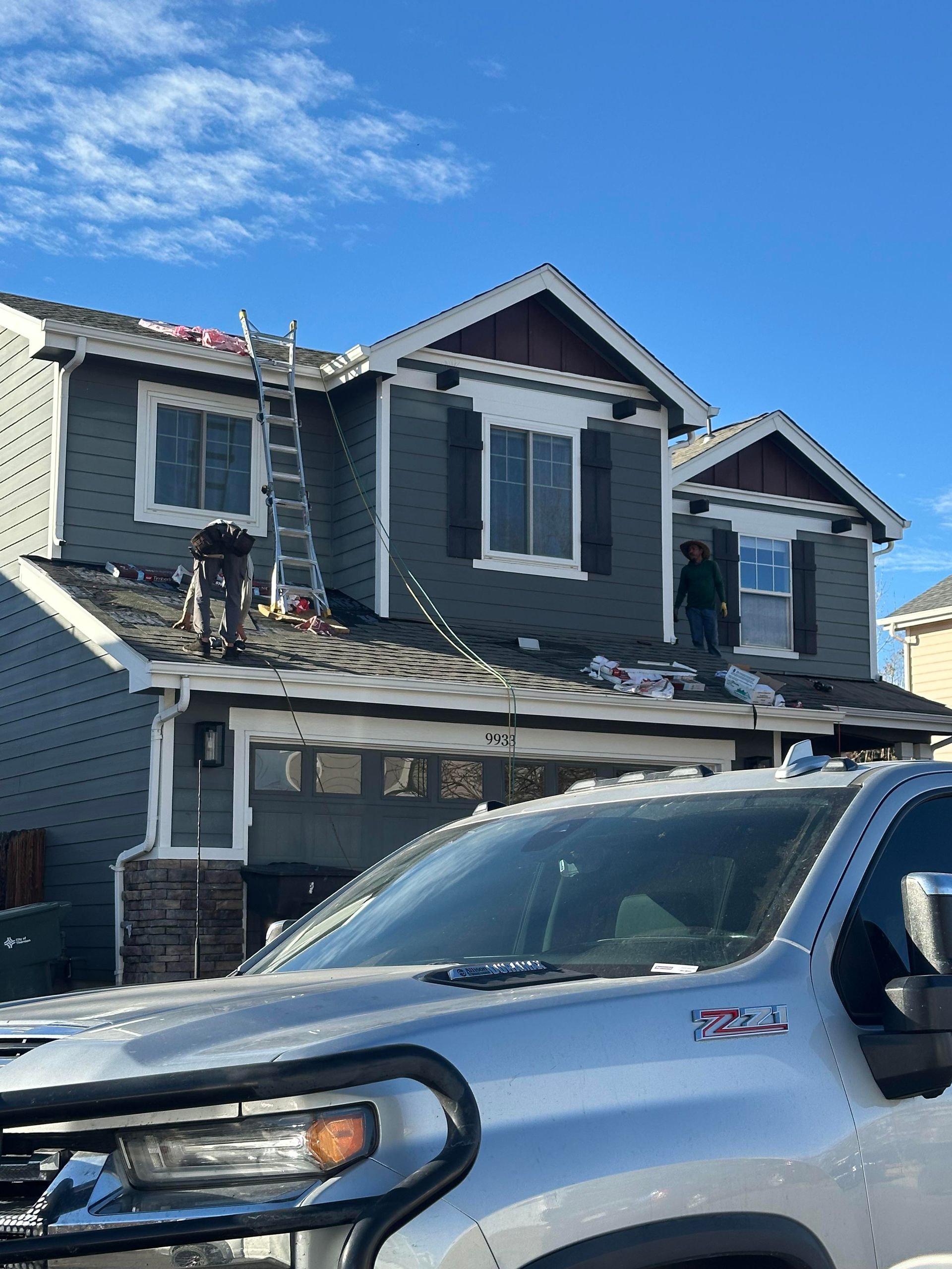 Two-story gray house with white trim and a silver pickup truck parked in front under a blue sky