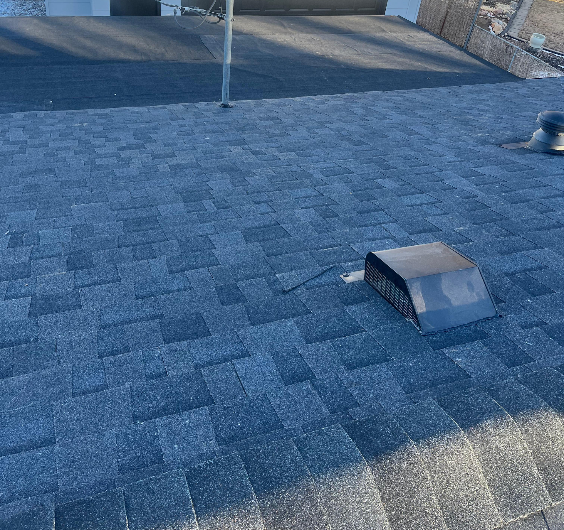 Blue shingled rooftop with a small metal vent and a pole near the top edge