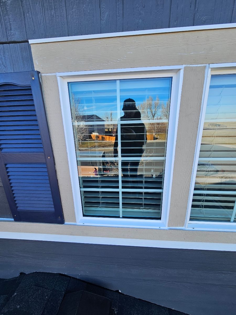Person reflected in a house window with white blinds and blue siding reflected sky