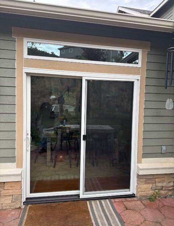 Backyard sliding glass door beneath a transom window on a beige house, with stone trim and a patio.
