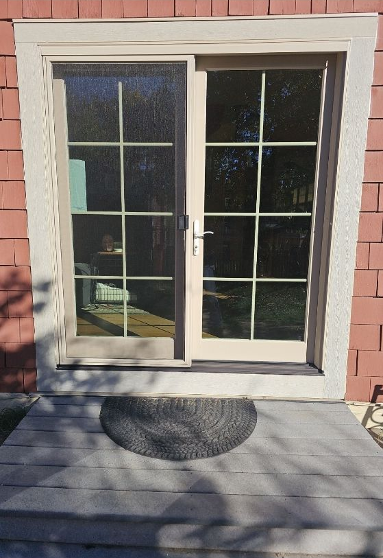 Sliding glass door with white frame, pink siding, and a dark doormat on a porch