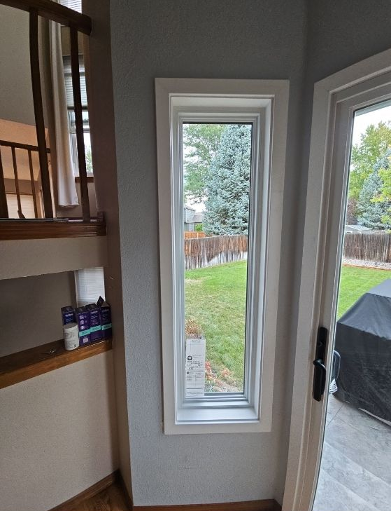 Kitchen corner with a narrow window overlooking a grassy yard and a covered grill outside.