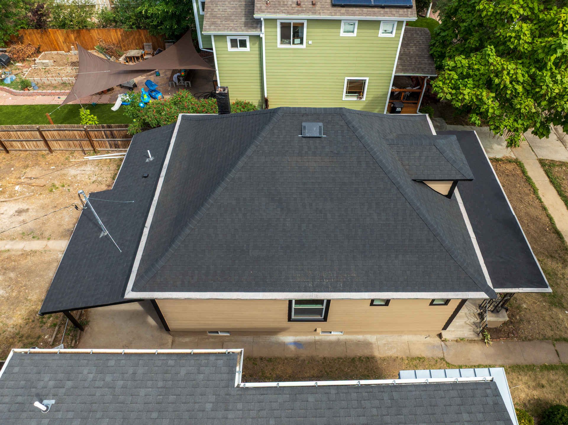 Aerial view of a tan house with a dark gray roof and fenced backyard in a residential neighborhood