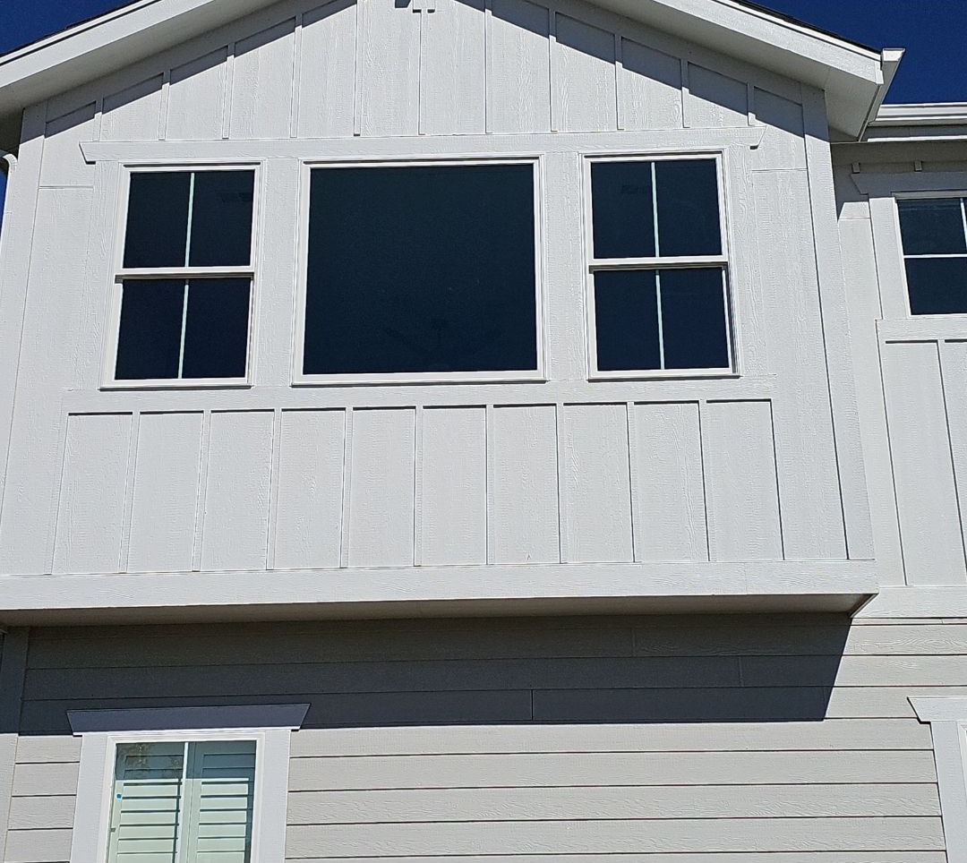 White house exterior with three upstairs windows and horizontal siding, seen in daylight