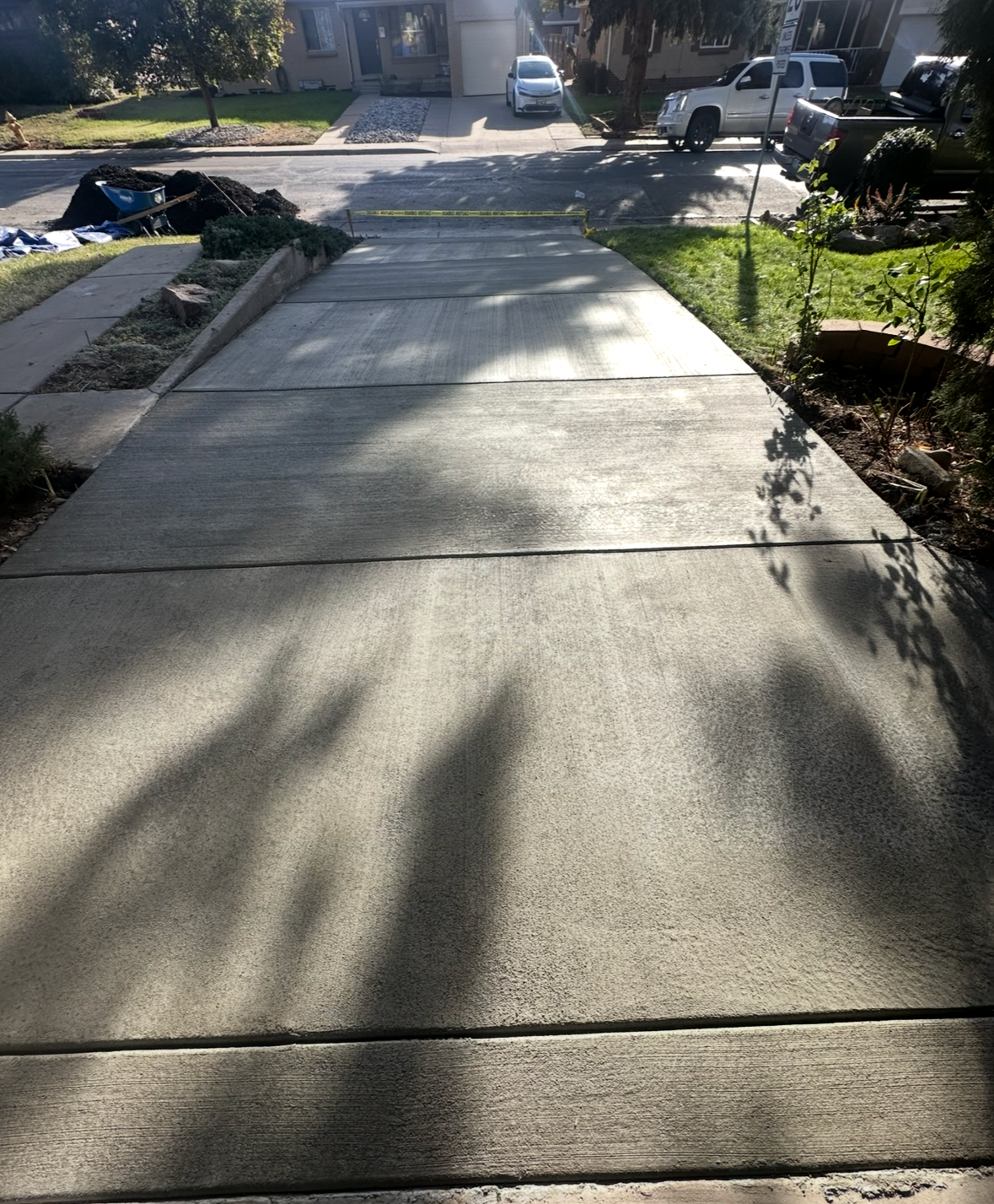 Sunlit concrete sidewalk with tree shadows beside a residential street and parked cars
