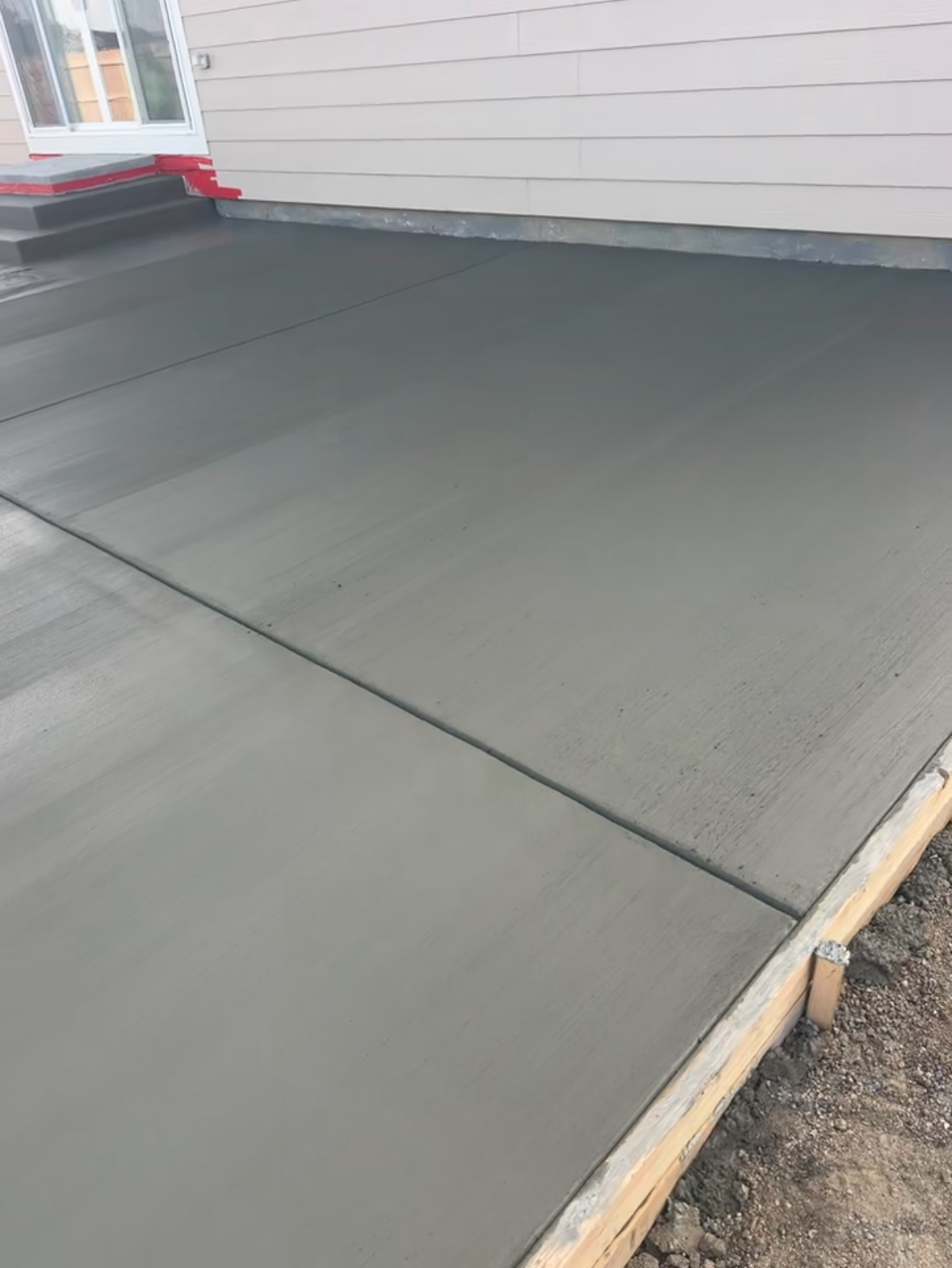 Freshly poured gray concrete porch slab beside a white house wall and steps