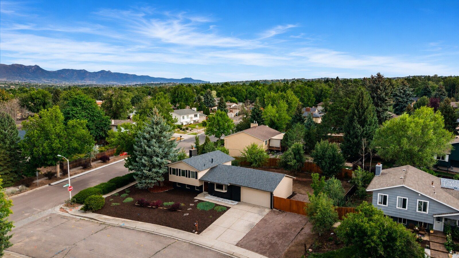 Aerial view of suburban homes and trees with mountains in the distance under a clear sky