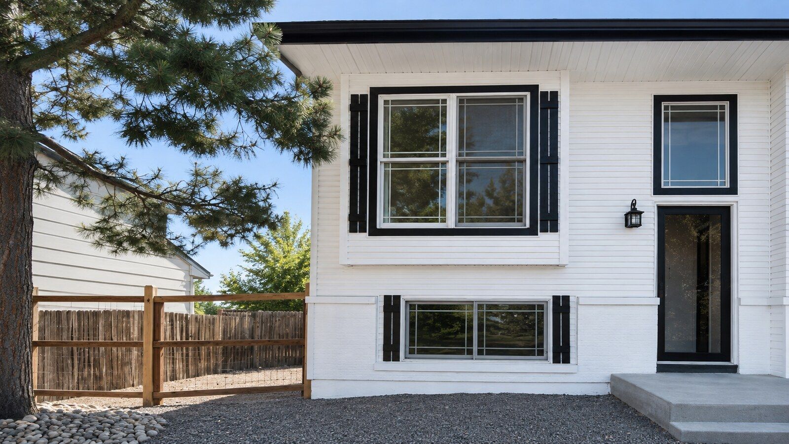 Front exterior of a white two-story house with black trim, a front door, windows, and gravel landscaping