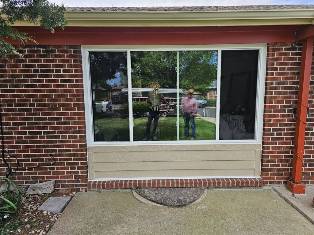 Brick house exterior with a large white-trimmed window reflecting a person and yard.