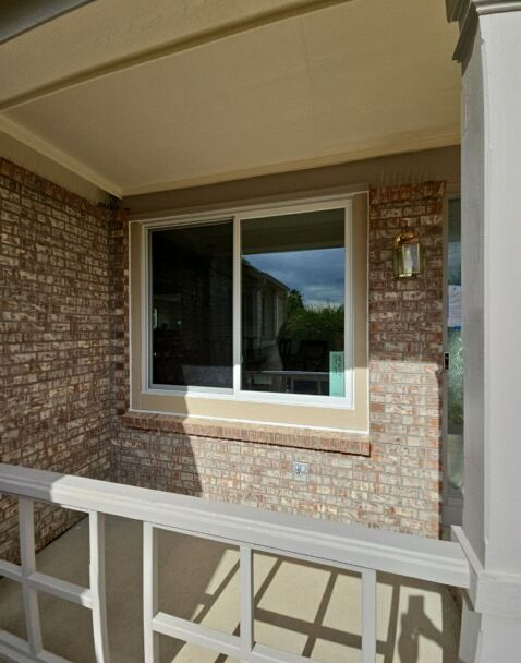 Brick house porch with a white-framed window and beige railing in sunlight