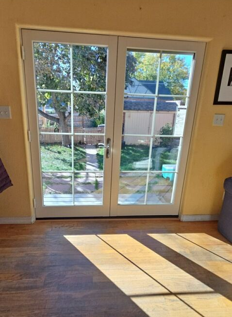 Sunlit living room with French doors opening to a backyard and long window shadows on the hardwood floor.