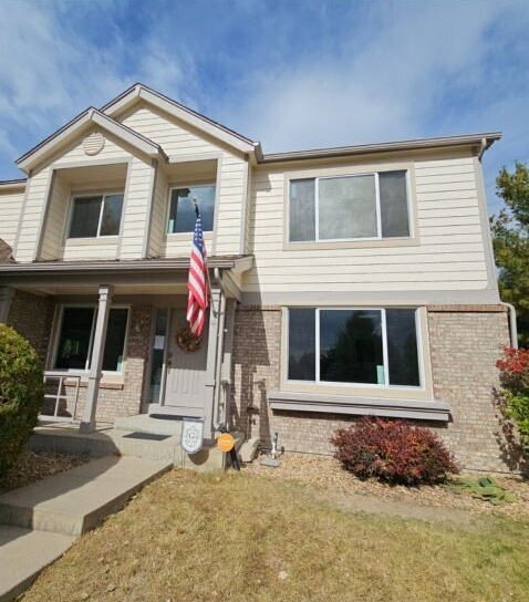 Two-story beige house with stone accents and an American flag by the front door